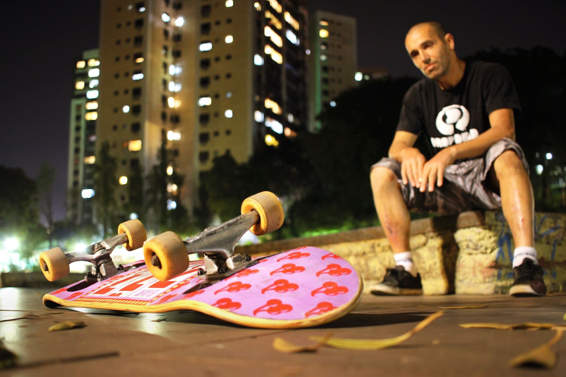 Tuka Porto sentado na pista da Orla à noite, com dois skates ao lado