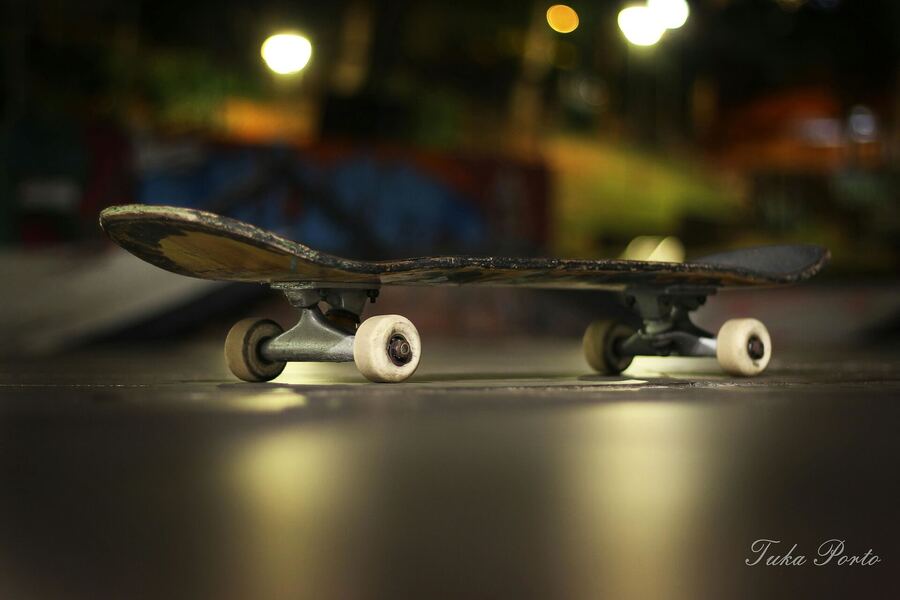 Close num skate no chão, com as luzes da noite ao fundo